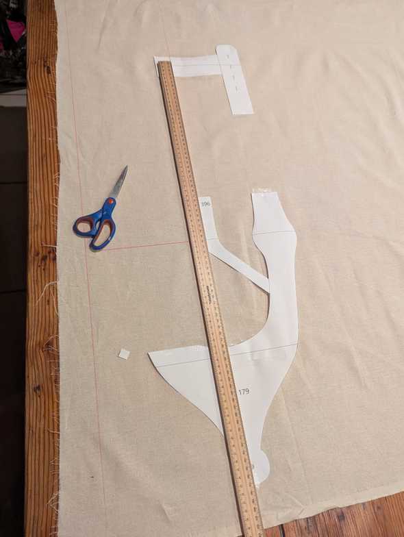 A photo of paper pattern cutouts taped down to calico, with a ruler being used for positioning along the centreline.