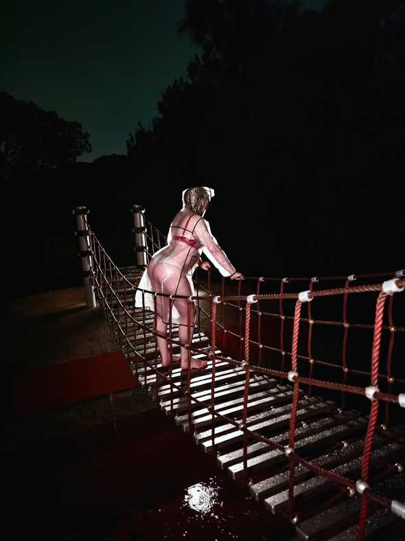 I'm standing on small rope bridge on a dark & stormy night. I'm wearing a clear raincoat, with only underwear underneath. I'm looking away from the camera, staring into the darkness. Backlighting has lit up the raincoat, forming a bright white halo around my body.