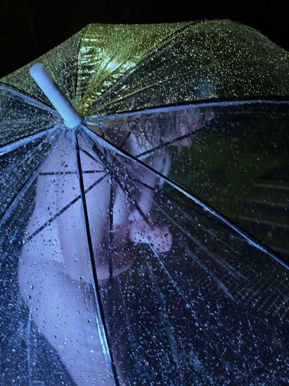 Close-up photo of me, naked behind the transparent umbrella. My pose suggests that I'm laughing in response to the discomfort of the cold.