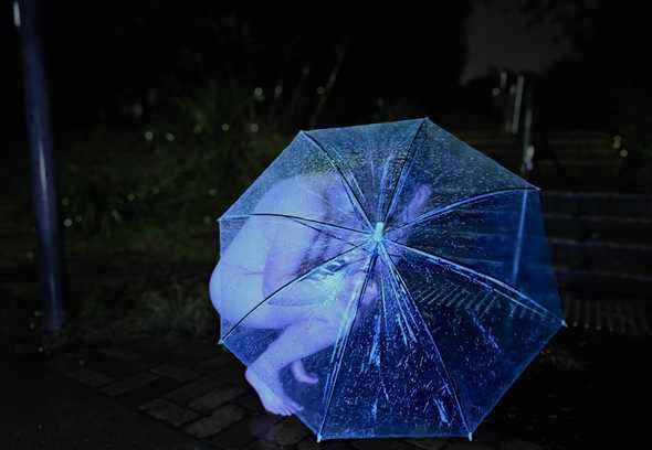 A photo of a dim walkway on a rainy night. Beneath the cold light of a lamp I cower. Completely naked, crouched low to the ground. I'm attempting to hide behind a transparent umbrella. It's not working. My tits are visible, my butt is visible, my bare feet are visible.